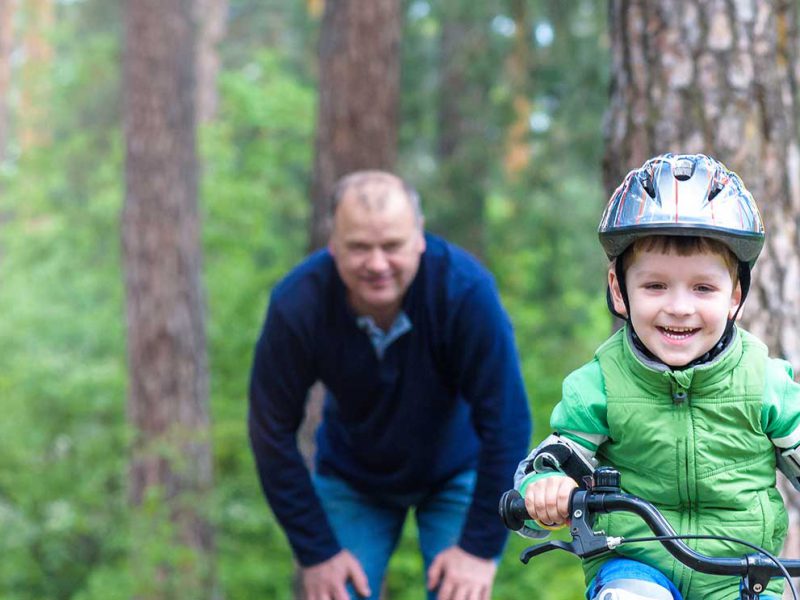 Caucasian child learning to ride bike with father in background