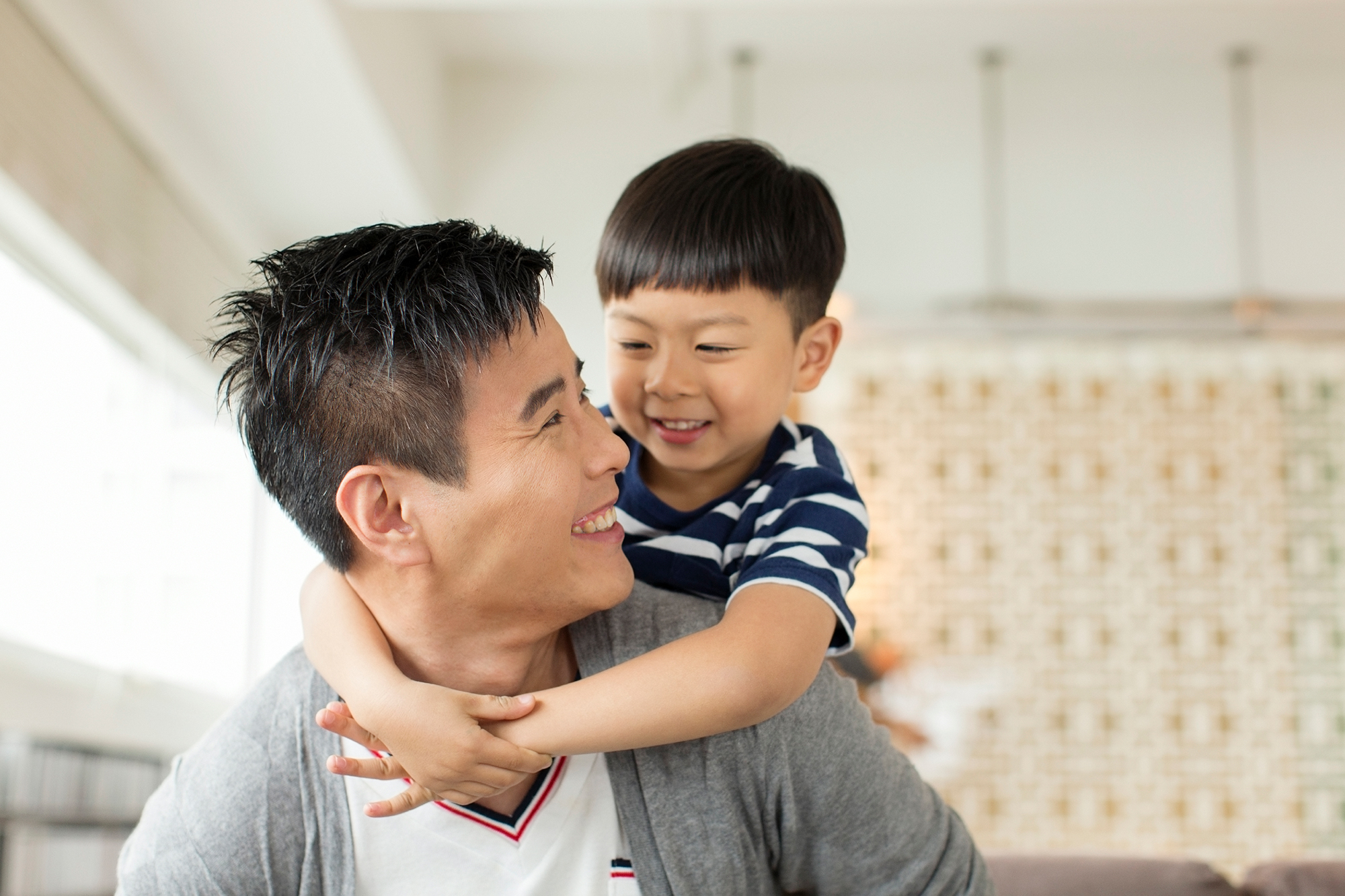 Asian father looking behind him at his son on his back - Indiana Fatherhood  Coalition